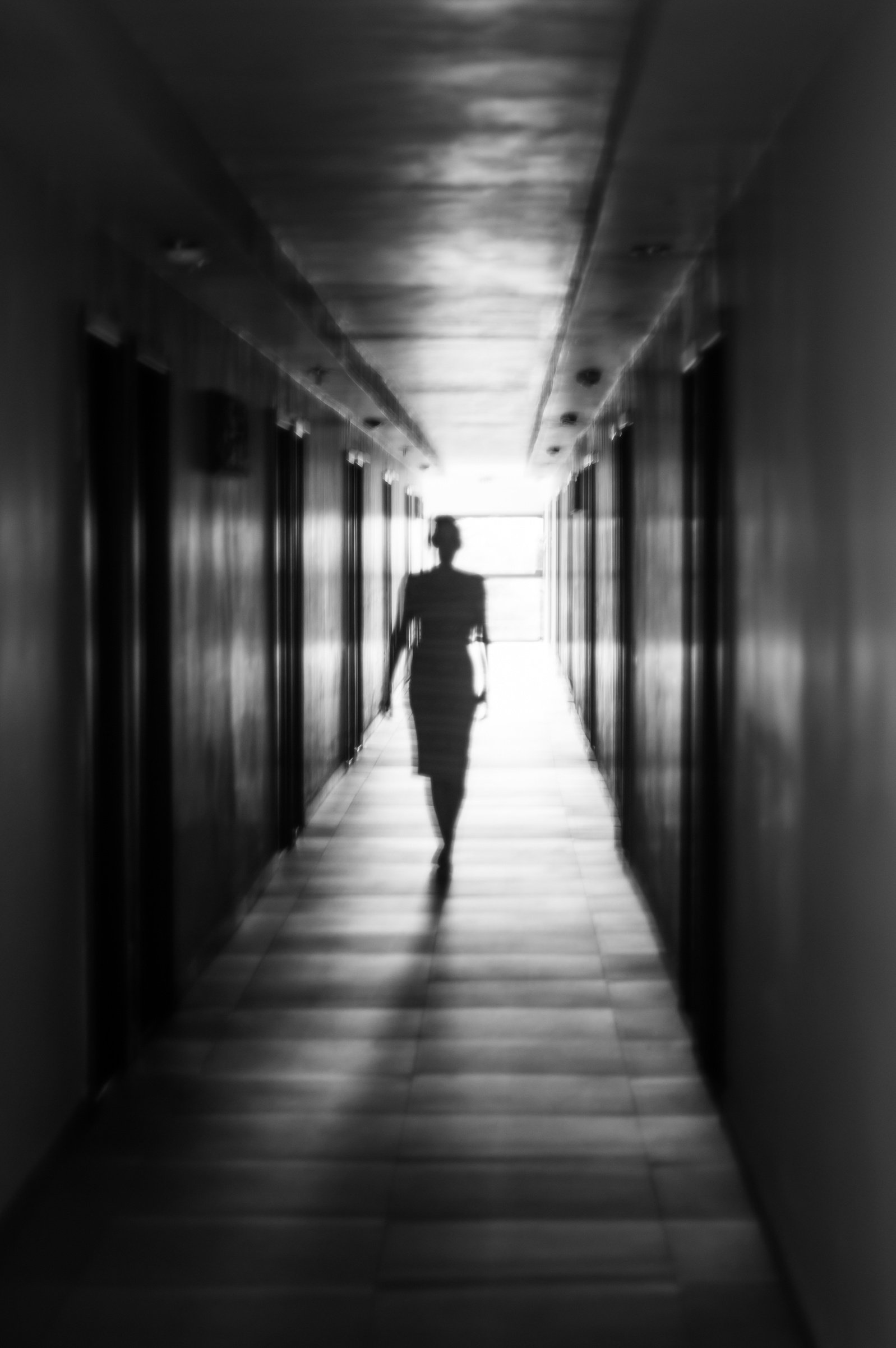 Ghostly silhouette walking down a creepy hallway, from light to shadow